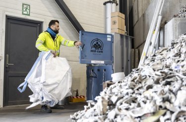 Worker loading an empty big bag into a baler